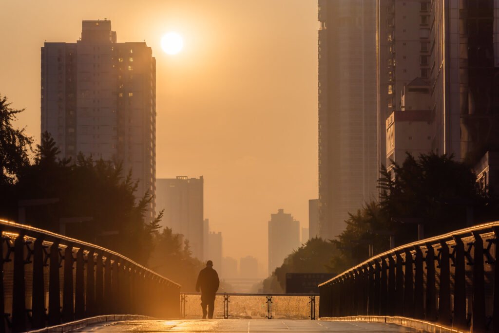Man walking on a foot bridge against sunrise in downtown Chengdu city