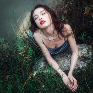 Portrait of a young woman in a silver dress lying on a rock in the middle of a lake