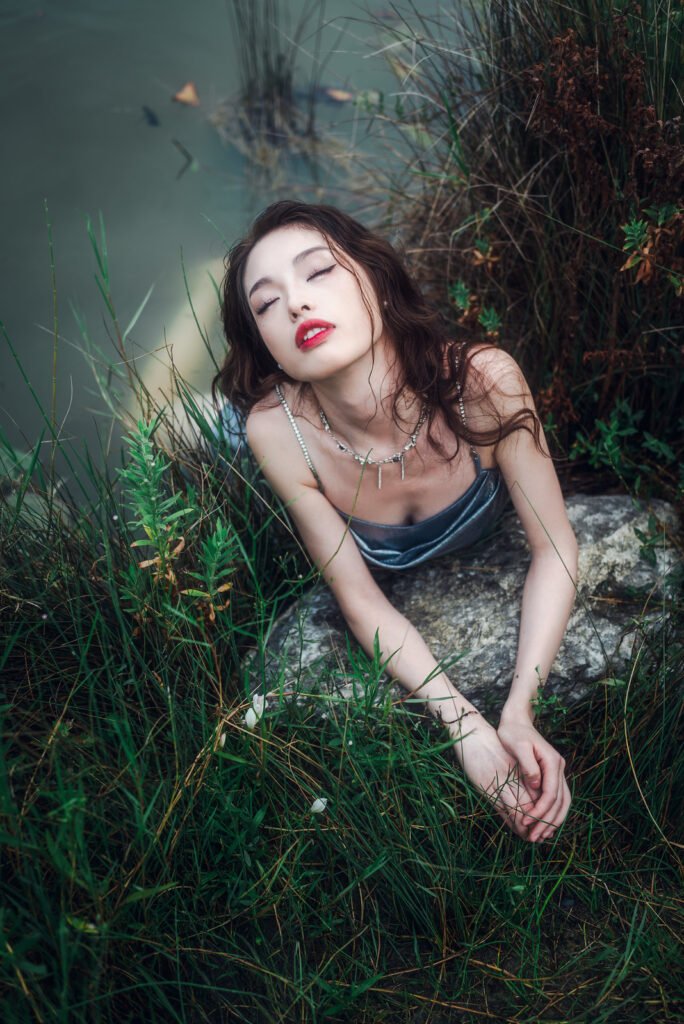 Portrait of a young woman in a silver dress lying on a rock in the middle of a lake