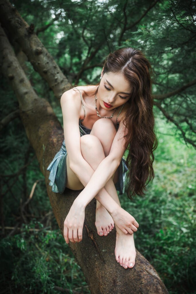 Young woman in silver dress sitting on a tree trunk in the forest