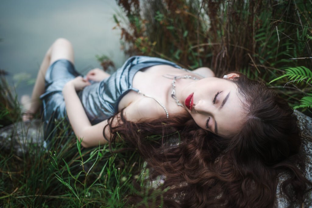 Beautiful woman in silver dress sleeping on rocks near the lake.