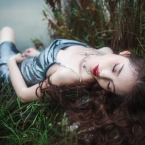 Beautiful woman in silver dress sleeping on rocks near the lake.