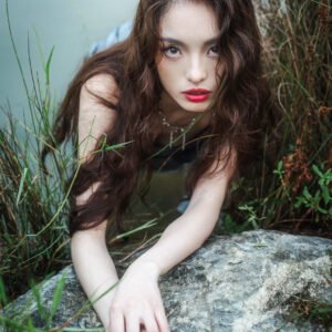 Portrait of a young woman in a silver dress lying on a rock in the middle of a lake