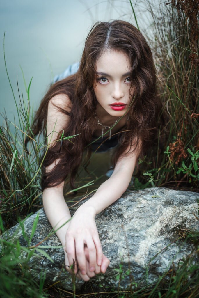 Portrait of a young woman in a silver dress lying on a rock in the middle of a lake