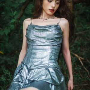 Young woman in silver dress sitting on a tree trunk in the forest