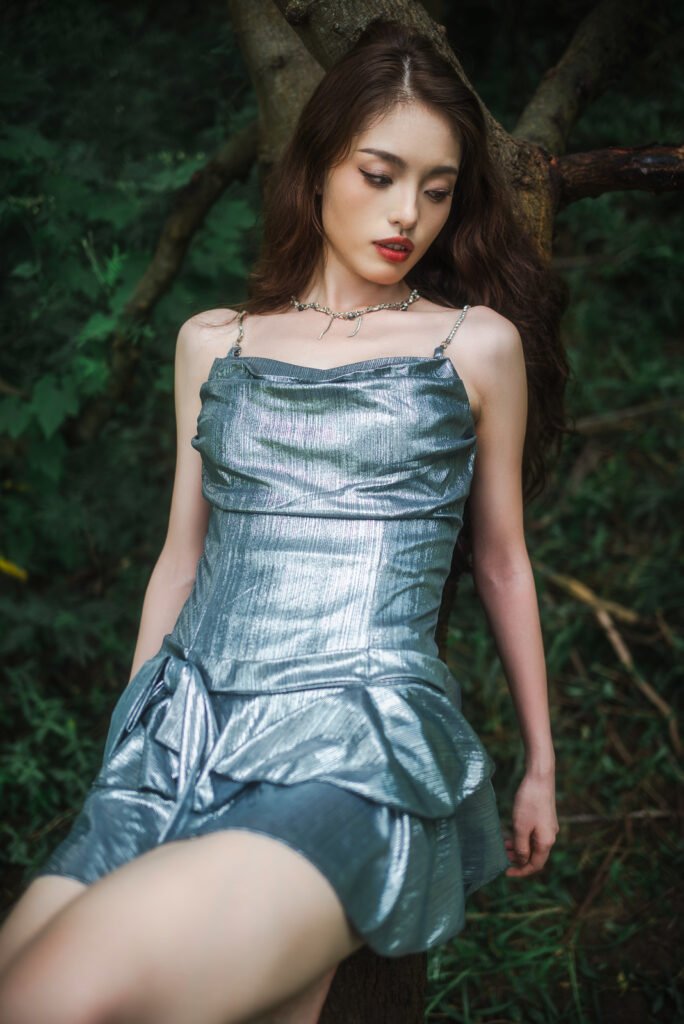 Young woman in silver dress sitting on a tree trunk in the forest