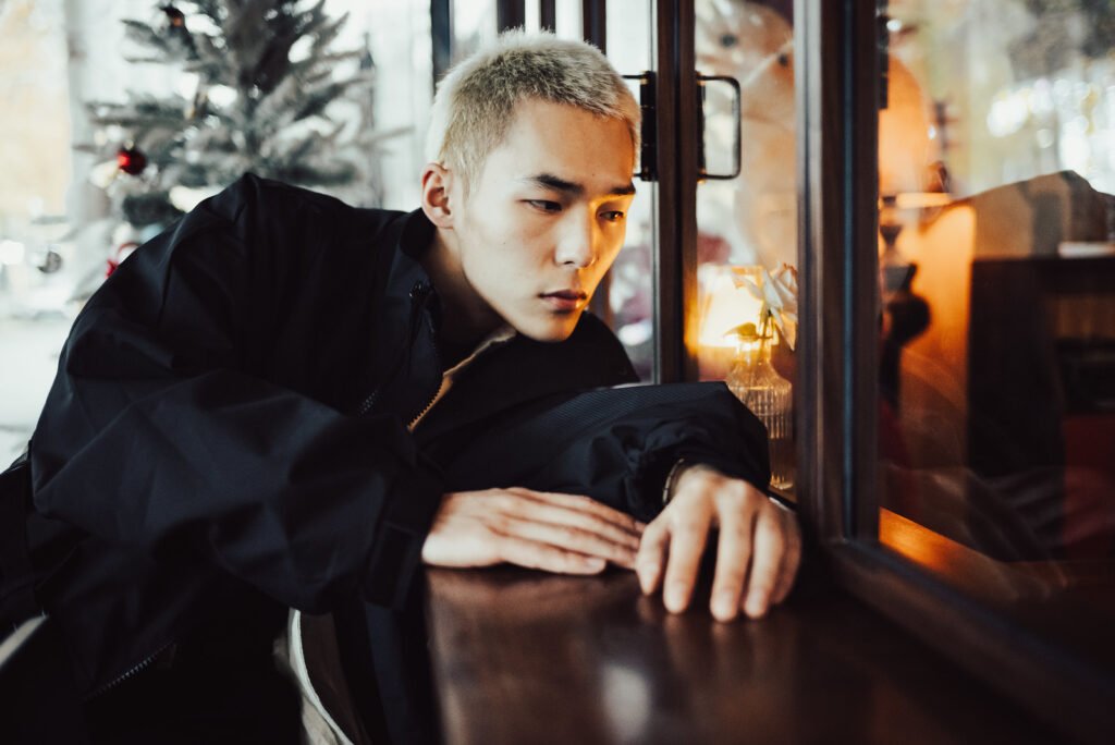 Portrait of a young man with short blond hair, looking out the window.