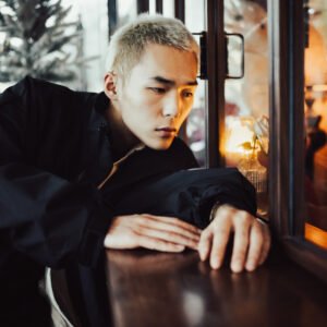 Portrait of a young man with short blond hair, looking out the window.