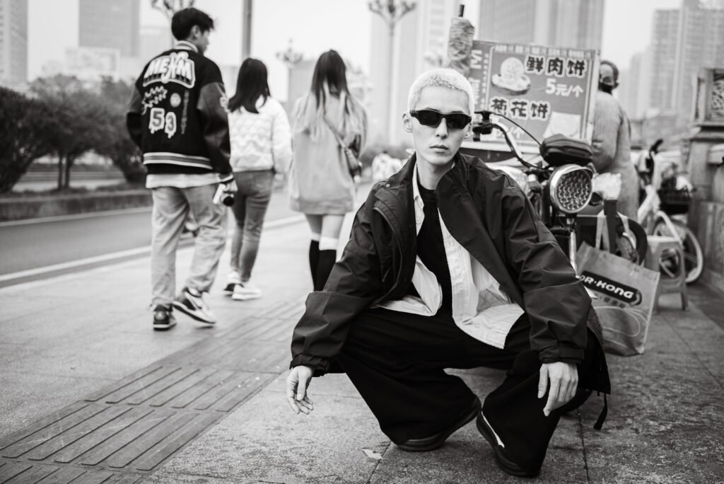 Young and stylish man crouching on the sidewalk in black and white