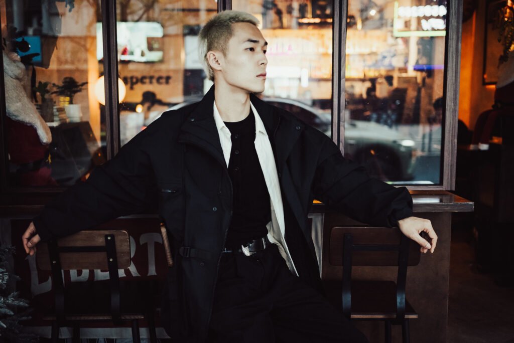 Young Asian man in stylish black clothes sitting in a cafe.