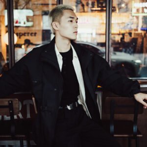 Young Asian man in stylish black clothes sitting in a cafe.