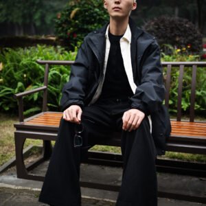 Young Asian man in stylish black outfit sitting on park bench.