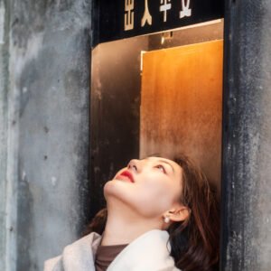 Young woman in a white sweater and gray scarf standing in front of a door.