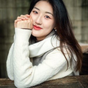 Beautiful Asian woman with long black hair wearing a white sweater smiling at the camera.