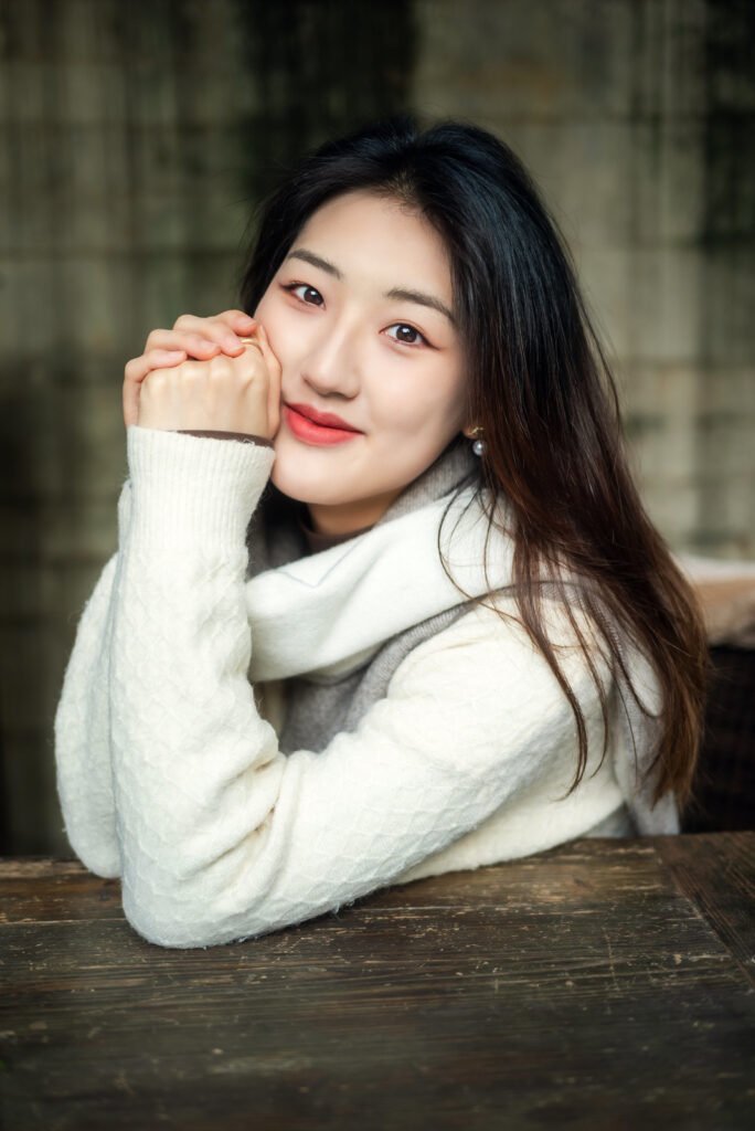 Beautiful Asian woman with long black hair wearing a white sweater smiling at the camera.