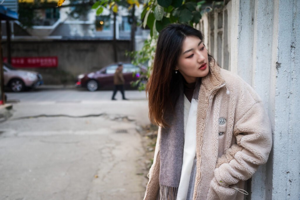 Young woman in a fur coat standing by the wall.