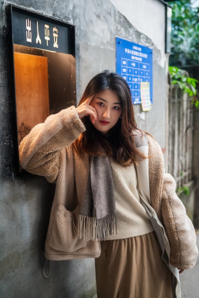 Young woman in a stylish winter outfit standing by a wall.