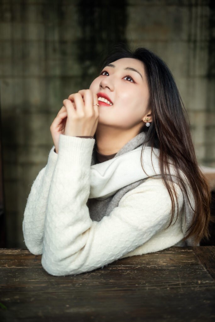 Young Asian woman in white sweater and gray scarf looking up and smiling.