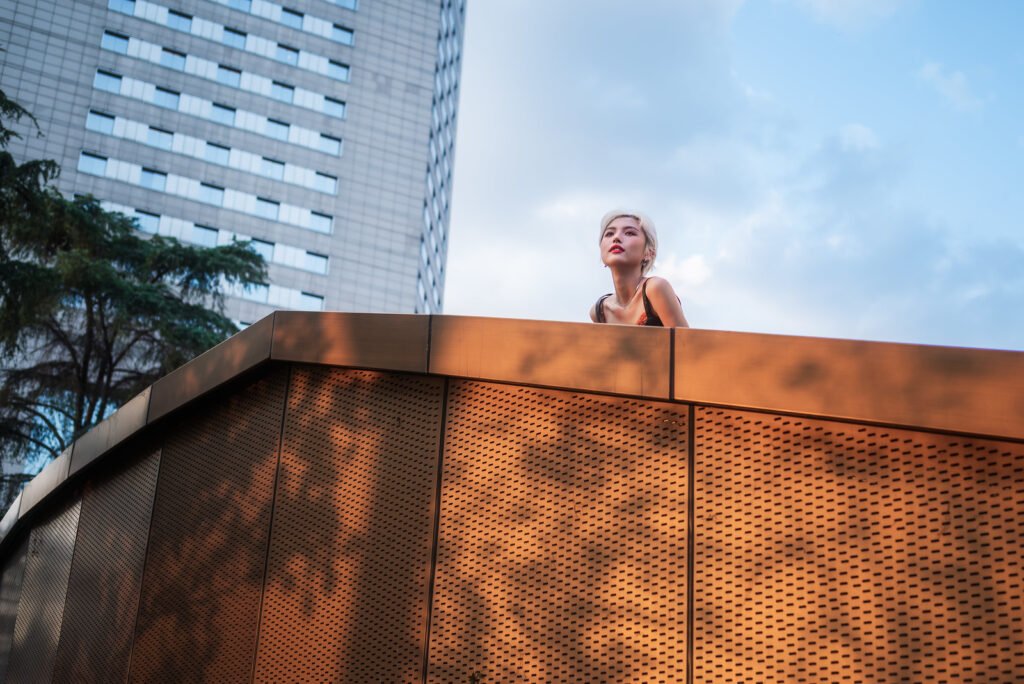 Blonde woman standing on a rooftop in front of a skyscraper.