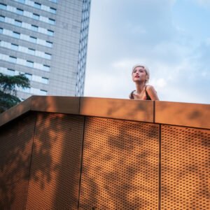 Blonde woman standing on a rooftop in front of a skyscraper.