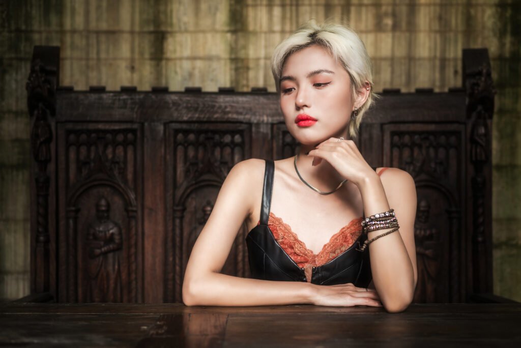 Blonde girl with red lips sitting at a table in front of a wooden background.