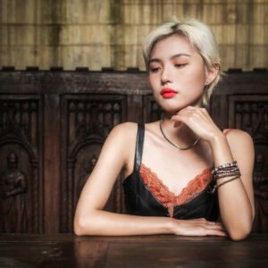 Blonde girl with red lips sitting at a table in front of a wooden background.
