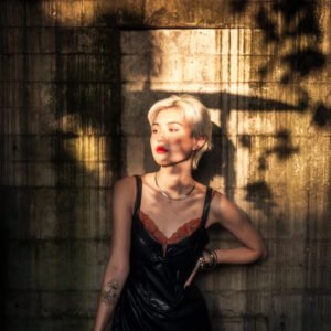 Blonde woman in black dress posing against concrete wall