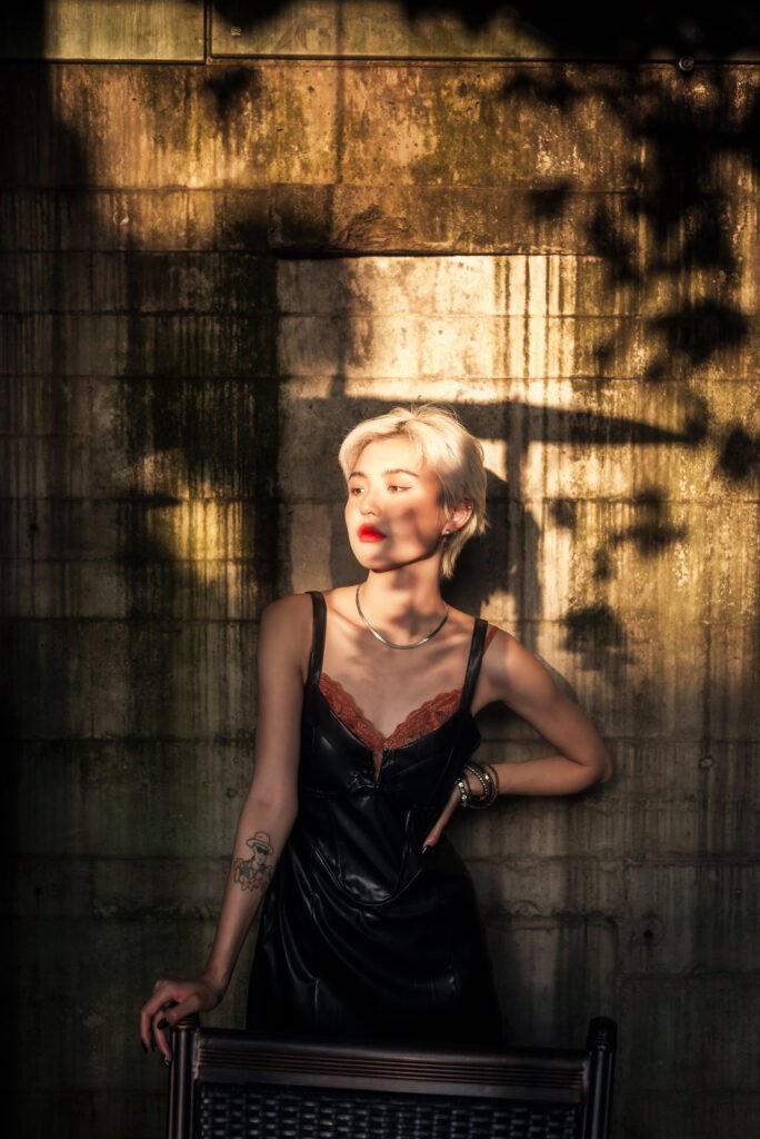 Blonde woman in black dress posing against concrete wall