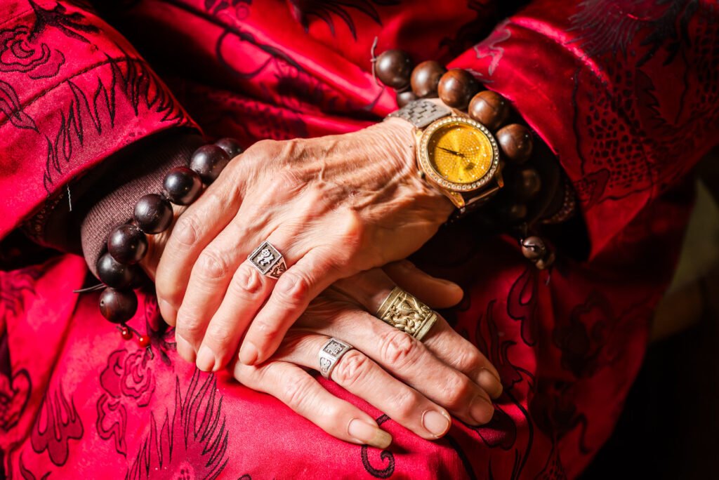 Elderly Chinese man wearing traditional Chinese clothing with a lot of jewelry on her hands.
