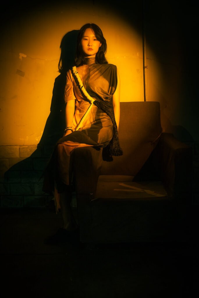 Young woman sitting on a armchair in a dark street with a spotlight on her.