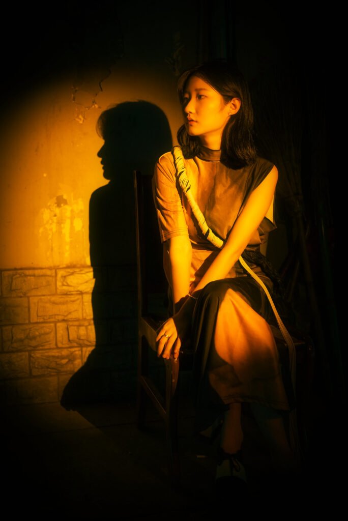 Young woman sitting on a armchair in a dark street with a spotlight on her.