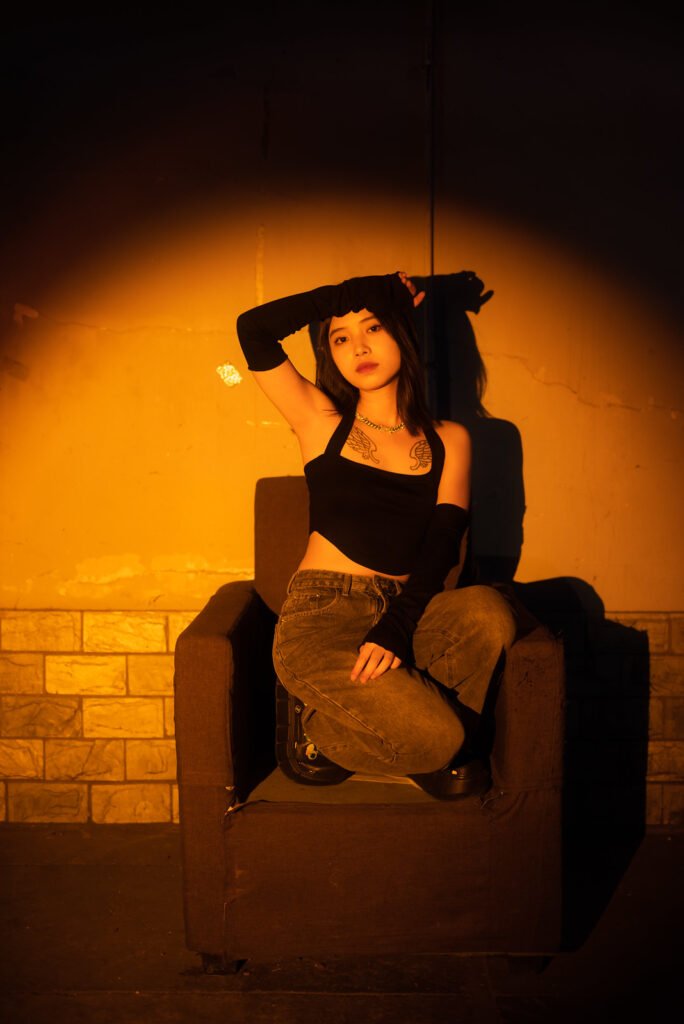 Young woman sitting on a armchair in a dark street with orange spotlight on her.