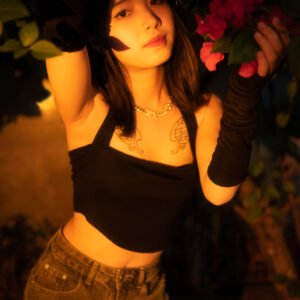 Young woman with tattoos and piercings posing in front of a bougainvillea bush.