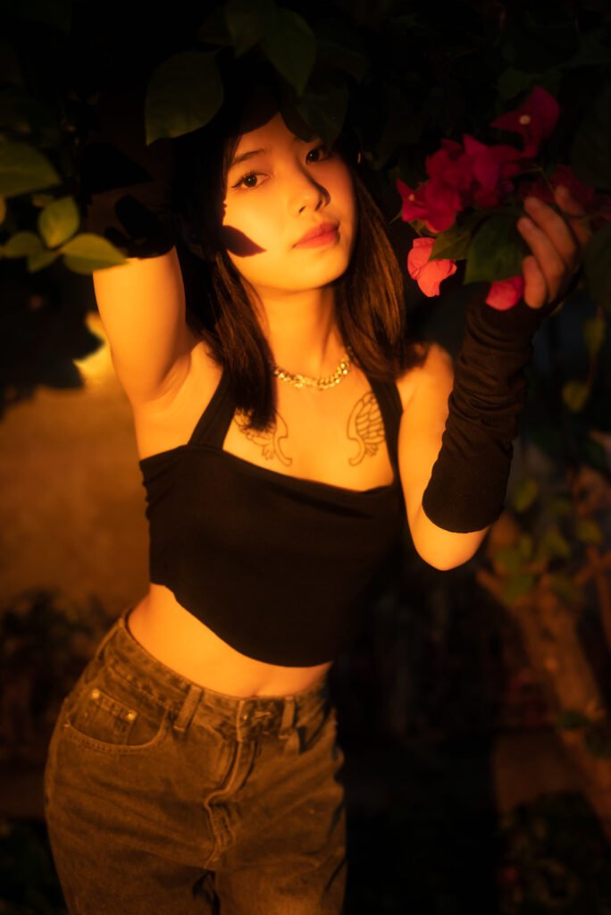 Young woman with tattoos and piercings posing in front of a bougainvillea bush.