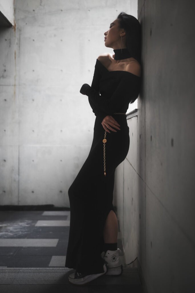 Young woman in black dress standing by the wall