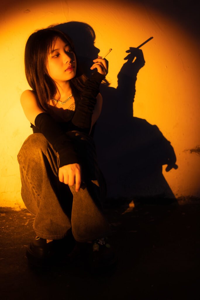 Young Chinese woman sitting in the street and smoking a cigarette portrait in a spotlight at night