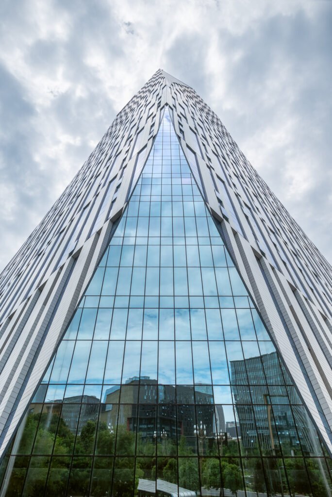 Modern skyscraper against cloudy sky with city reflecting on the glass facade