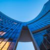 Modern curved glass skyscraper facade reflecting clear blue sky at night