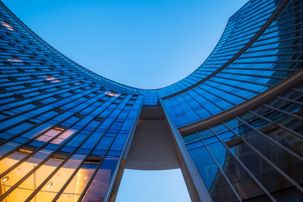 Modern curved glass skyscraper facade reflecting clear blue sky at night