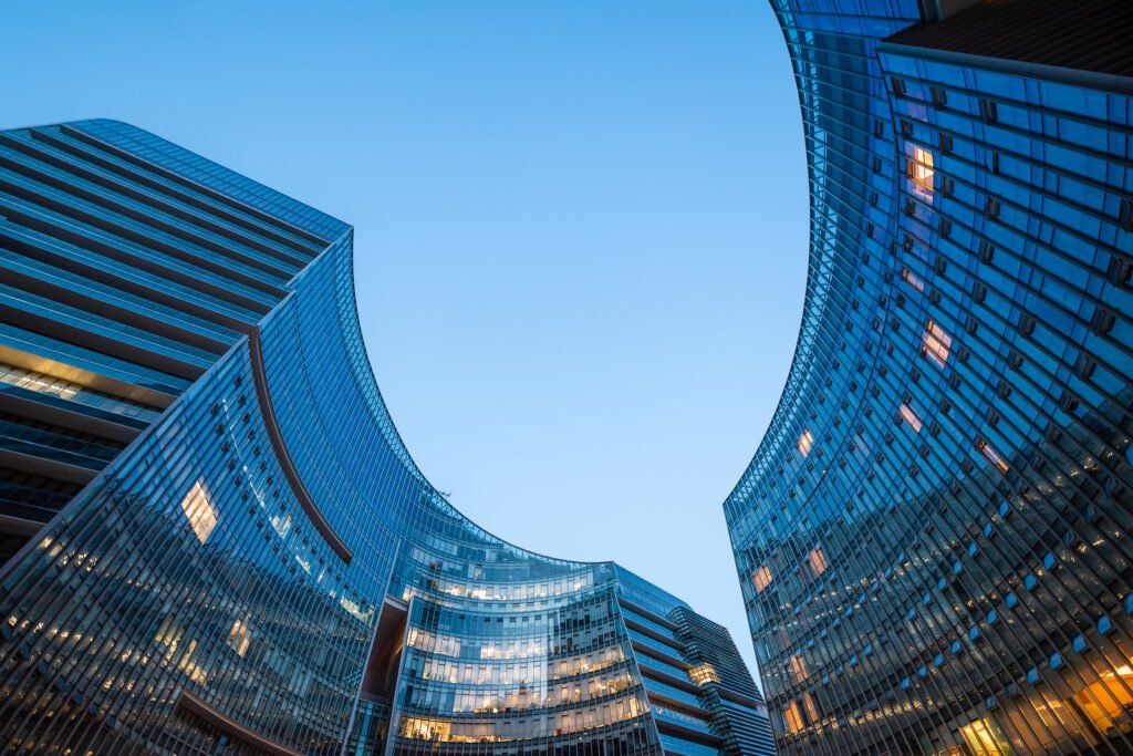 Modern curved glass skyscrapers facade reflecting clear blue sky at night