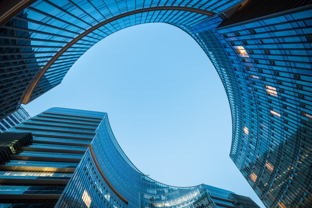 Modern curved glass skyscrapers facade reflecting clear blue sky at night