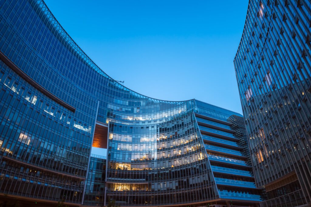 Modern curved glass skyscrapers facade reflecting clear blue sky at night