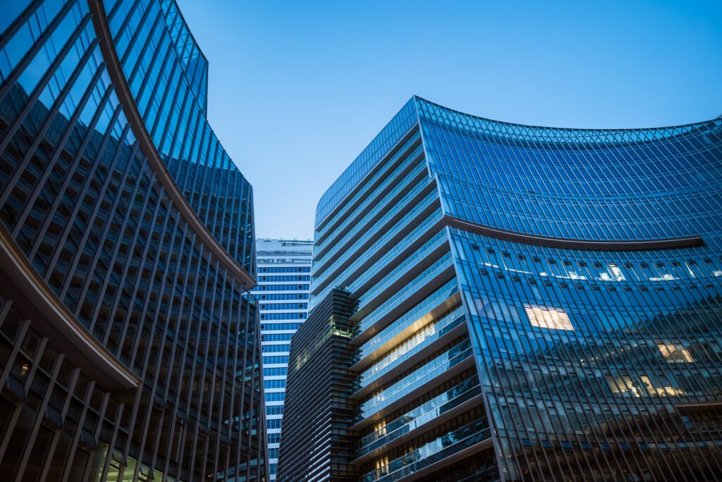 Modern curved glass skyscrapers facade reflecting clear blue sky at night