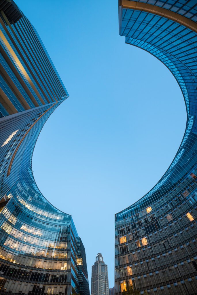 Modern curved glass skyscrapers facade reflecting clear blue sky at night