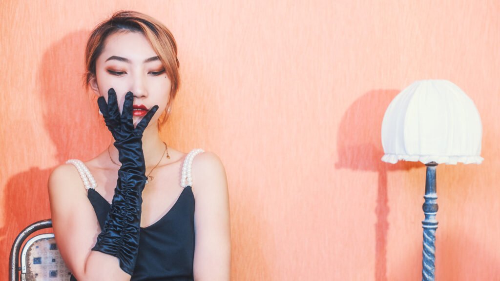 Young woman in black dress and gloves sitting by a lamp.