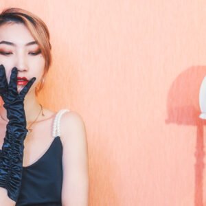 Young woman in black dress and gloves sitting by a lamp.