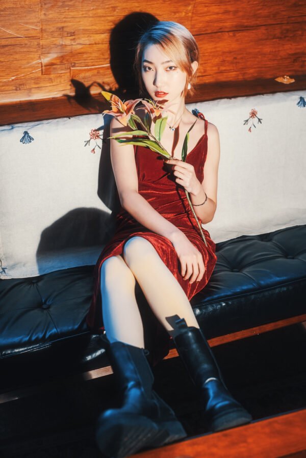 Young woman in red dress sitting on a couch holding a lily flower