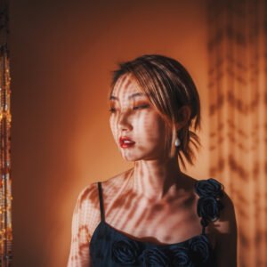 Portrait of a young woman standing in front of a curtain with sunlight and shadow on her face and body.